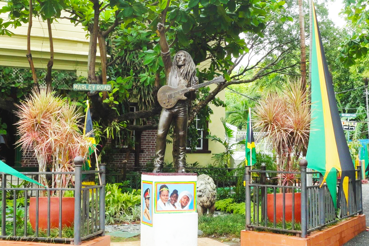 Bronze statue of Bob Marley standing at the front yard of his former Hope Road home, now a museum, holding his famous guitar and captured in a lively pose that reflects his reggae spirit.