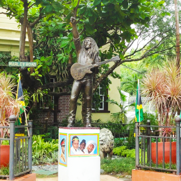 Bronze statue of Bob Marley standing at the front yard of his former Hope Road home, now a museum, holding his famous guitar and captured in a lively pose that reflects his reggae spirit.