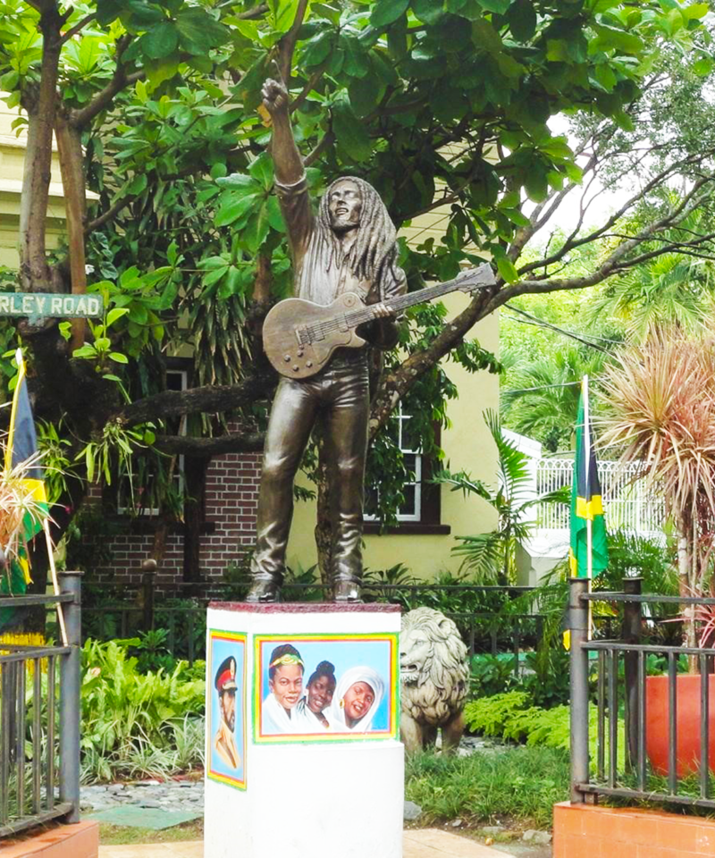 Bronze statue of Bob Marley standing at the front yard of his former Hope Road home, now a museum, holding his famous guitar and captured in a lively pose that reflects his reggae spirit.