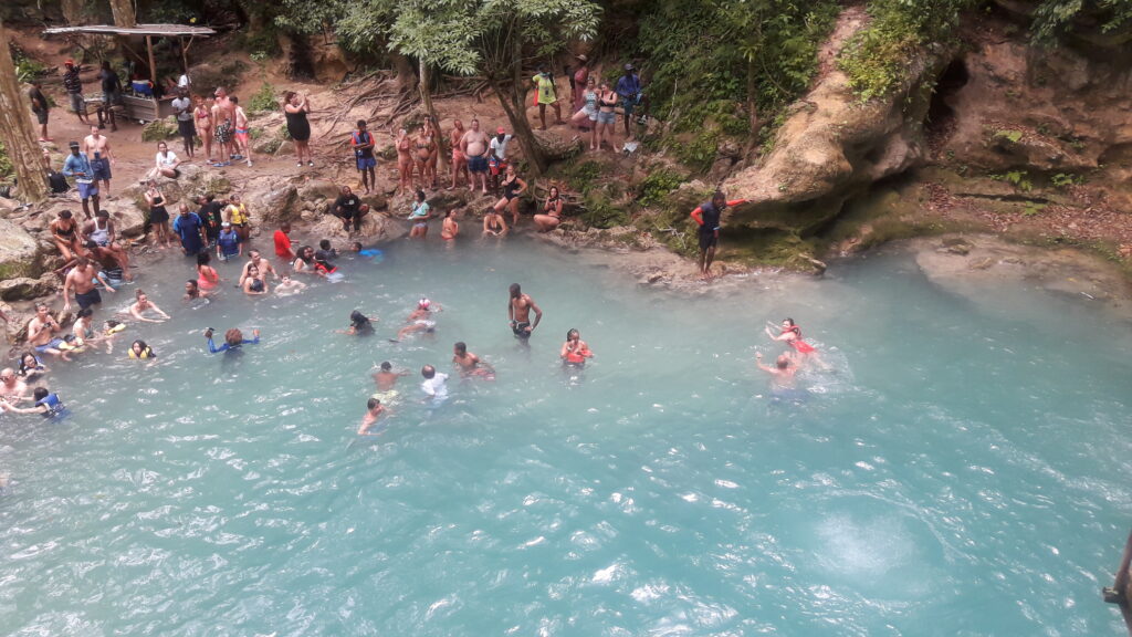 Overhead view of visitors swimming in the Blue Hole River as others sit and stand on surrounding rocks