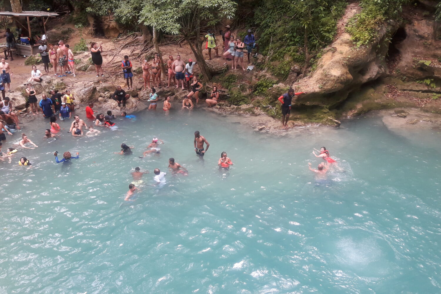 Overhead view of visitors swimming in the Blue Hole River as others sit and stand on surrounding rocks