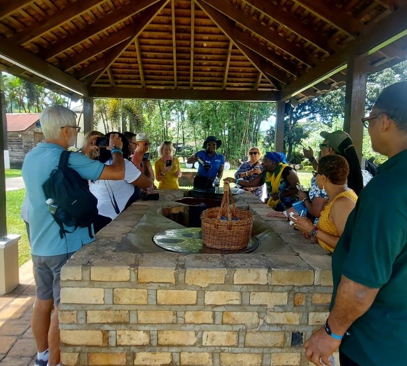 Visitors gathered around inside the molasses station at Appleton Estate, listening to a tour guide explain the history of molasses making while receiving samples to taste.