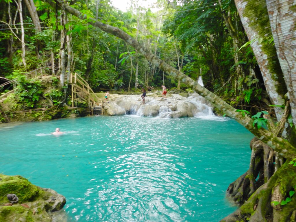 Visitors climb rocks with a guide along Blue Hole river, deep blue water flowing behind.