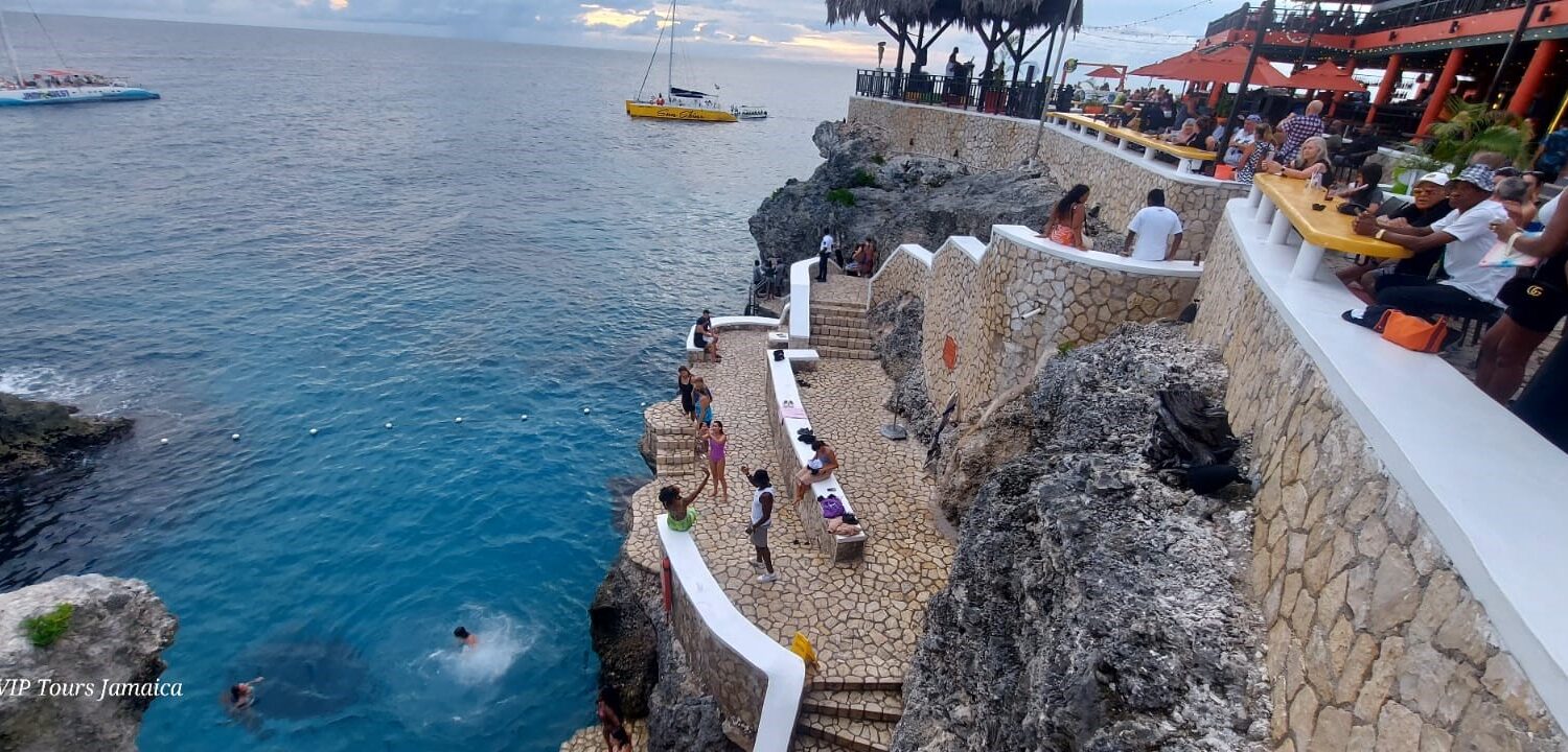 Visitors leap from the base of the cliff at Rick’s Café in Negril, Jamaica, while others watch from the cliffside and boats anchored offshore add to the lively Caribbean scene.