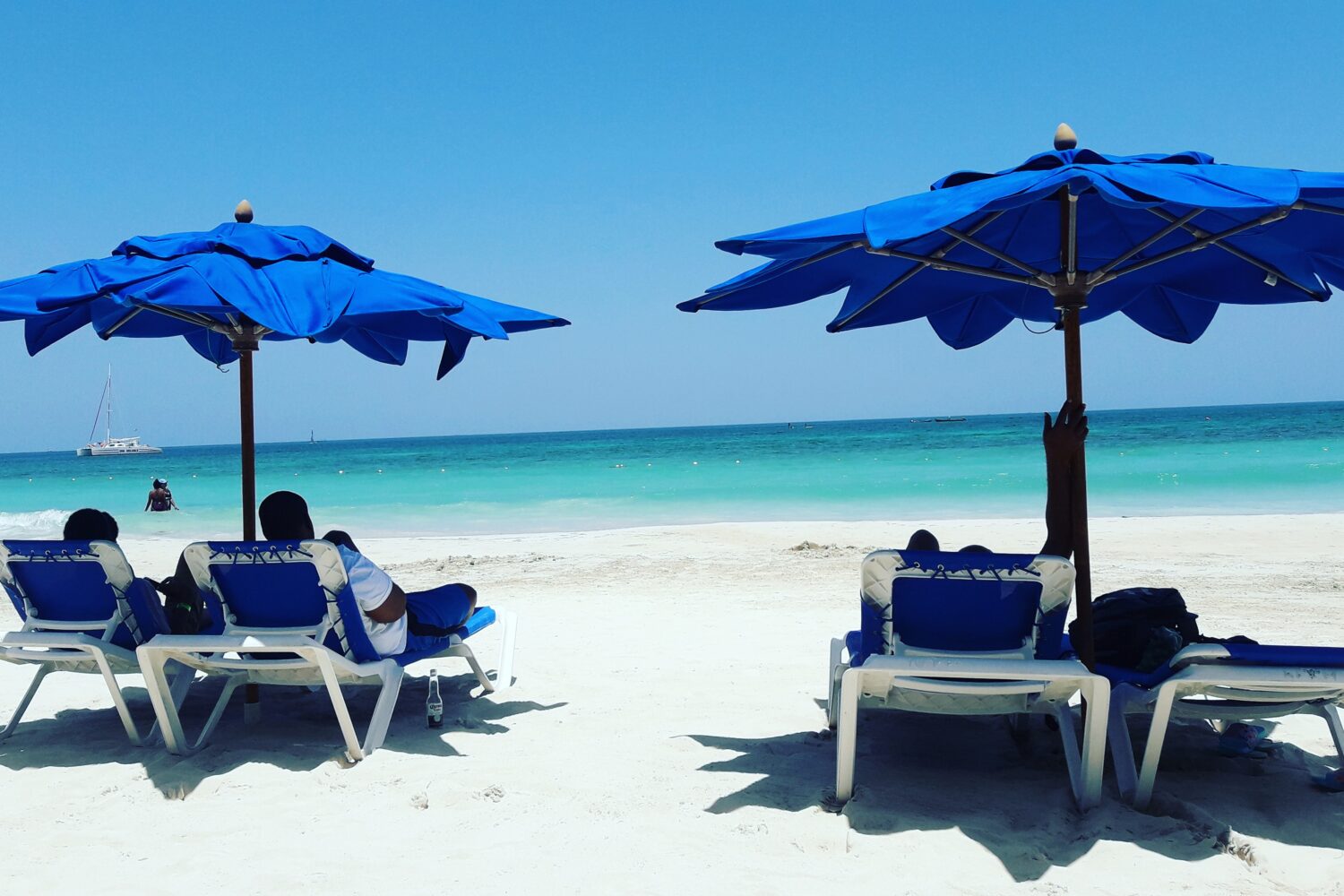 Visitors relax on Negril’s sandy beach beneath colorful umbrellas, enjoying the Caribbean sun and sea breeze