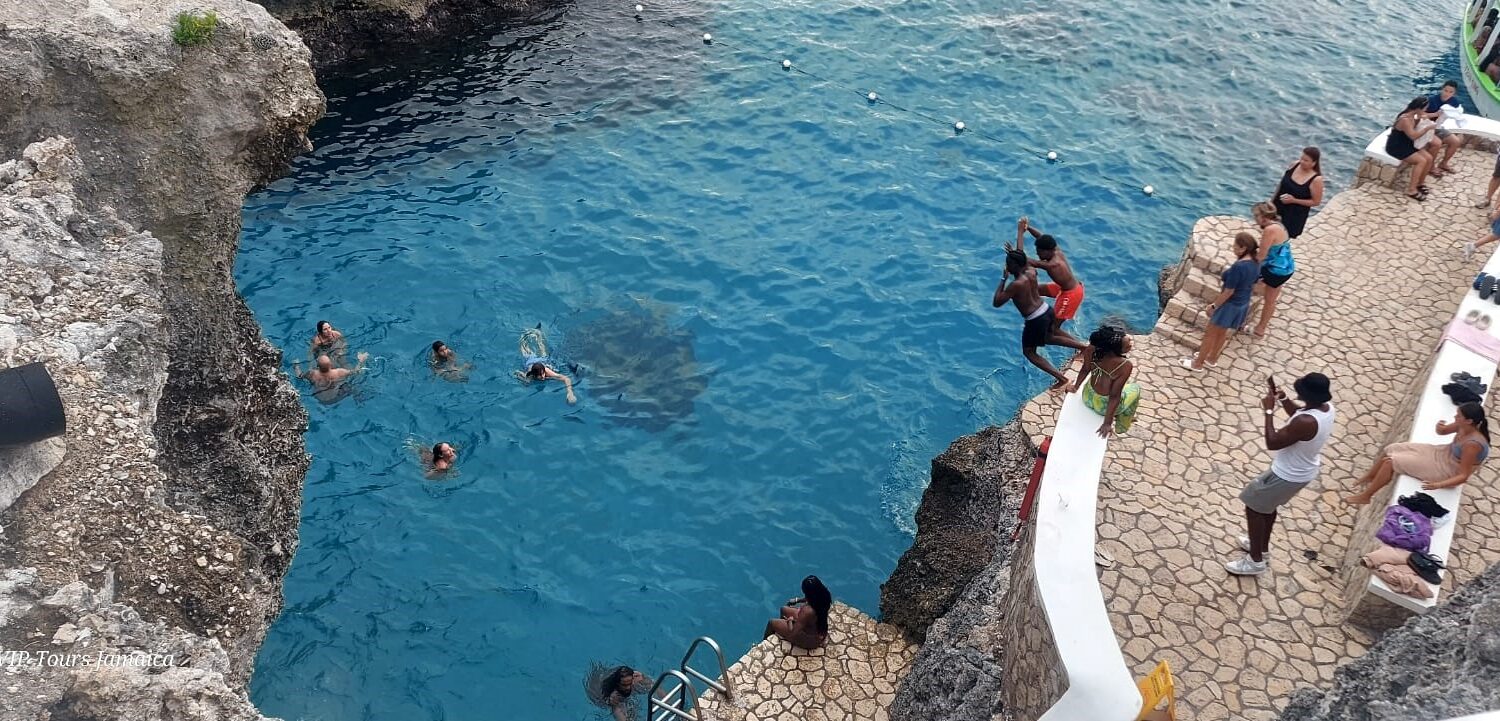 Visitors leap from the base of the cliff at Rick’s Café in Negril, Jamaica, while others watch from the cliffside and boats anchored offshore add to the lively Caribbean scene.