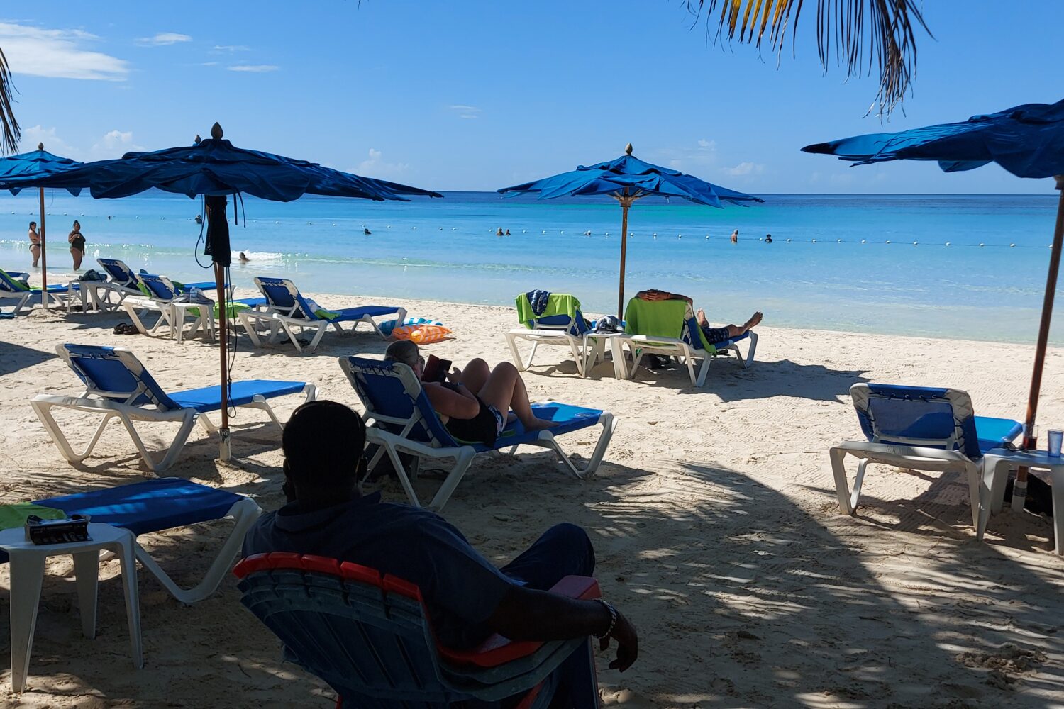 Visitors relax on Negril’s sandy beach beneath colorful umbrellas, enjoying the Caribbean sun and sea breeze