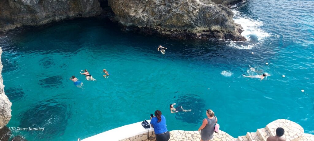 People swimming in the deep blue water with huge rocks. People looking on