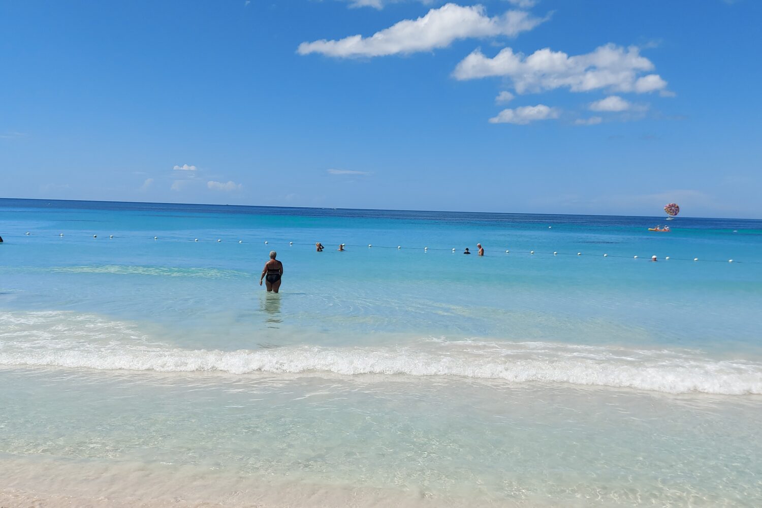 Visitors stand and stroll along the water’s edge on Negril’s Seven Mile Beach, enjoying the Caribbean shoreline