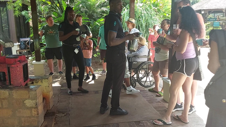 Several visitors stand at the sugarcane mill holding glasses as the tour guide and staff share freshly squeezed sugarcane juice, pressed moments earlier by two guests from the group.