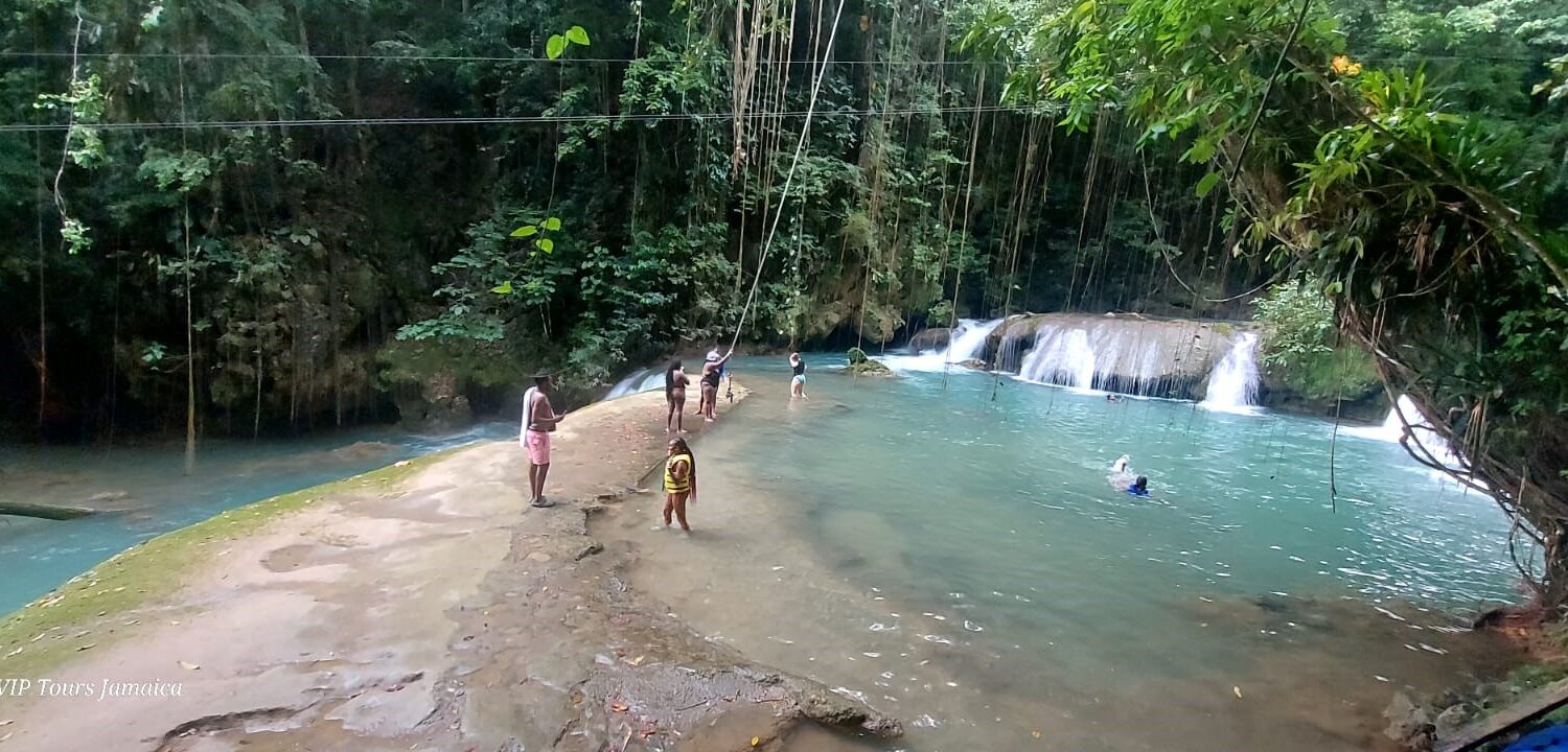 Two people standing on the rocks at YS Falls taking photos of the cascading waterfall