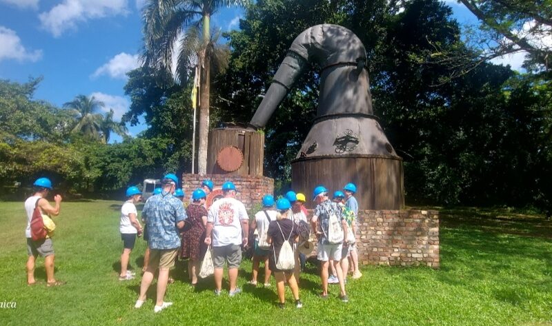 Group of visitors wearing hard hats gathered around a tour guide at Hampden Estate in Trelawny, listening to information about historic pot stills used in rum production.