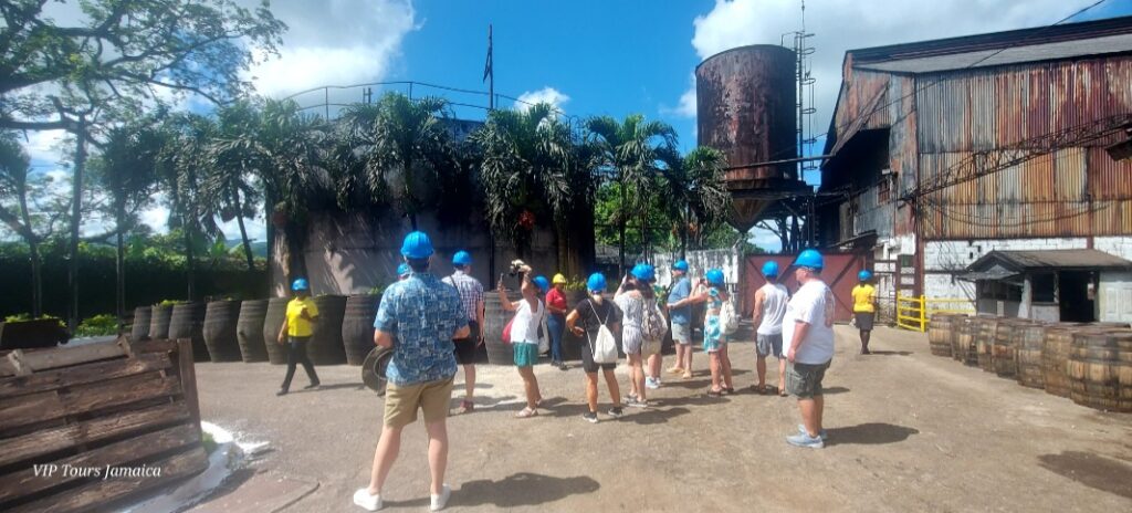 Group of visitors wearing hard hats touring the Hampden Sugar Estate factory in Trelawny, observing machinery and production areas.