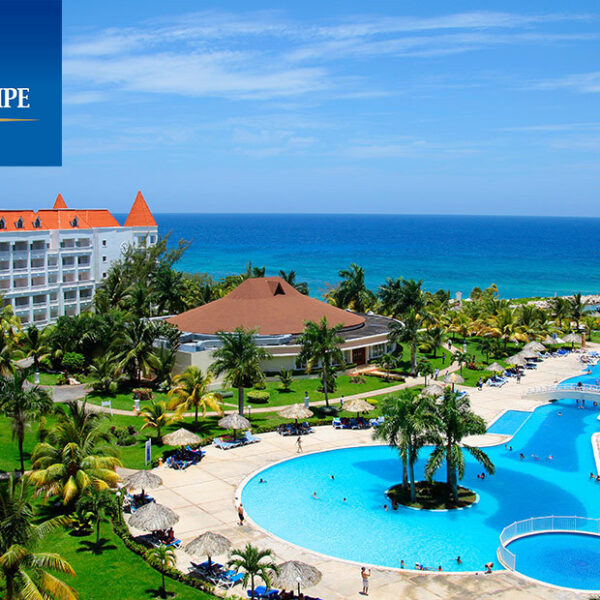 Panoramic view of the Grand Bahia Principe Resort in Jamaica with elegant white buildings, lush palm trees, turquoise swimming pools, and the sparkling Caribbean Sea beyond, creating a serene tropical atmosphere.